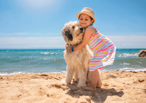 niña en la playa abrazando a su perro